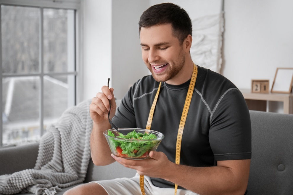 ozempic-and-testosterone-young-man-with-tape-measure-around-his-neck-eating-salad-at-home