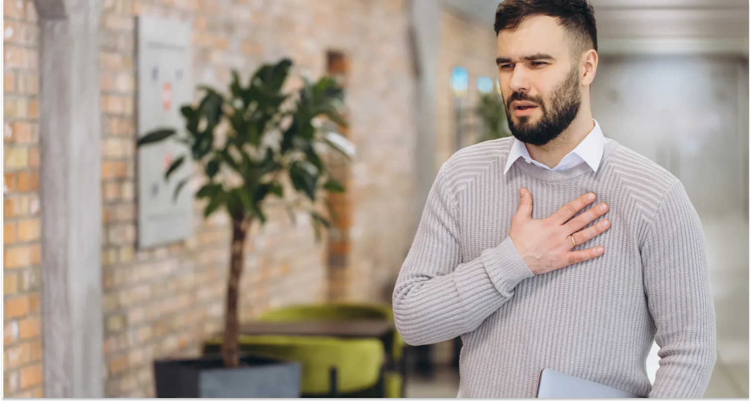 A man experiencing acute chest pain, standing in an office and holding a laptop.