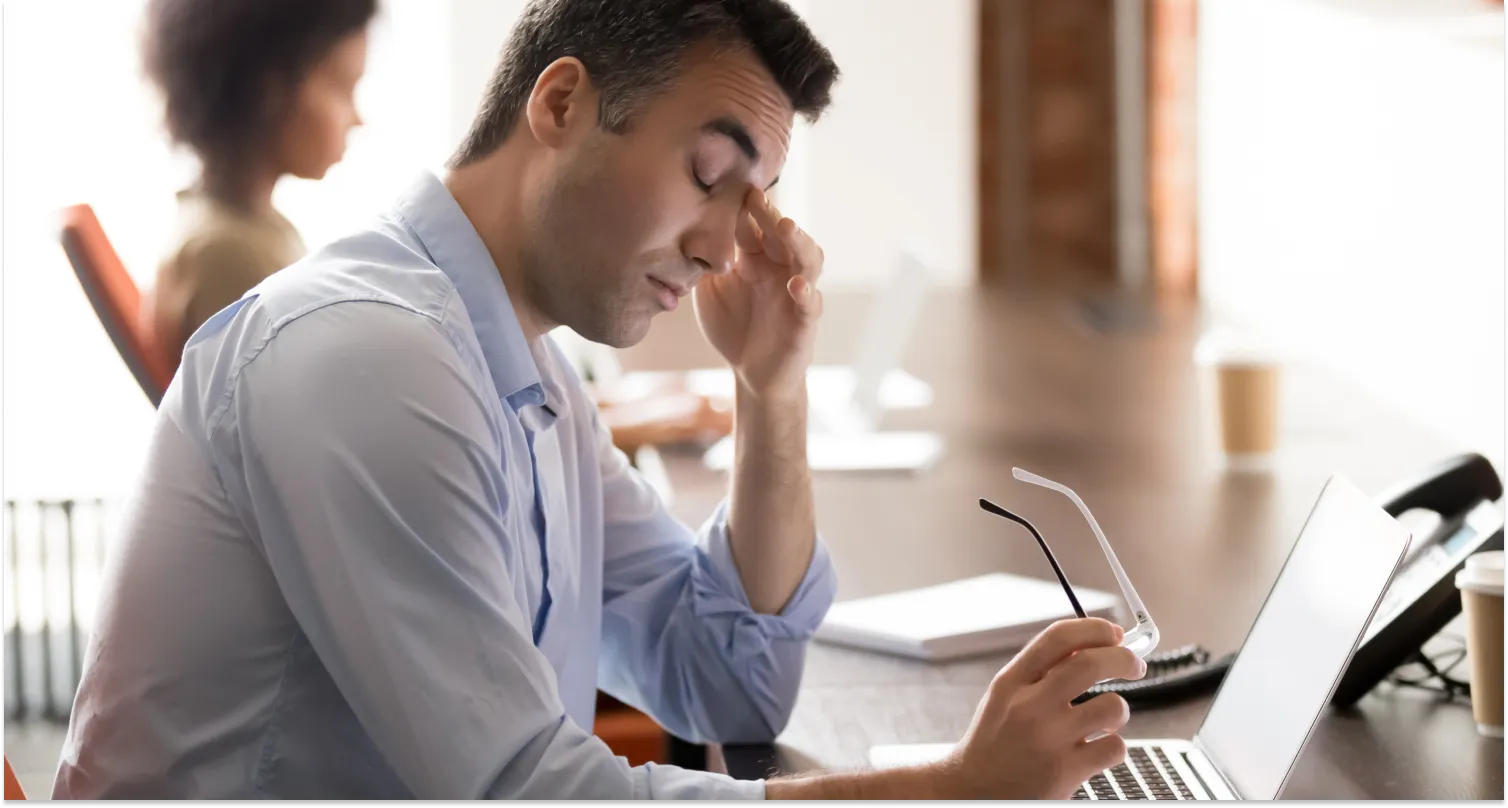 A tired stressed middle-aged businessman holding glasses, his mood changing to feeling irritable.